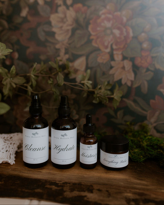 Set of skincare: Cleanse, Hydrate, Moisturize, Everything Balm in front of a dark floral wallpaper