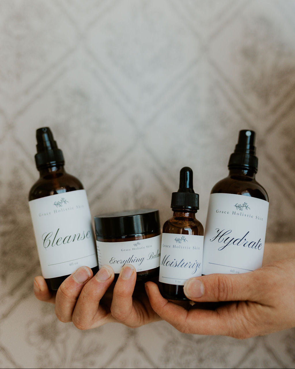 Cleanse, hydrate, moisturize, and everything balm, held in hands in front of textured wallpaper